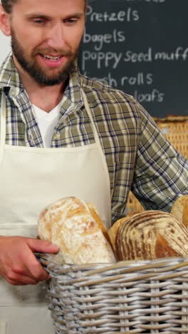 Portrait-of-male-staff-holding-breads-in-basket-at-bakery-section