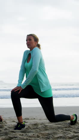 Mature-couple-performing-stretching-exercise-on-beach