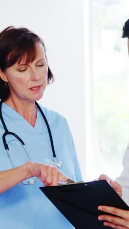 Nurse-and-doctor-discussing-over-clipboard-in-corridor