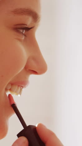 Woman-applying-lip-gloss-on-her-lips-in-bathroom