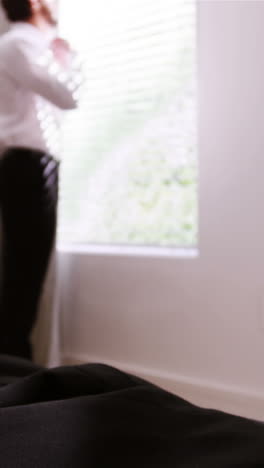 Man-getting-dressed-while-looking-through-window-in-bedroom