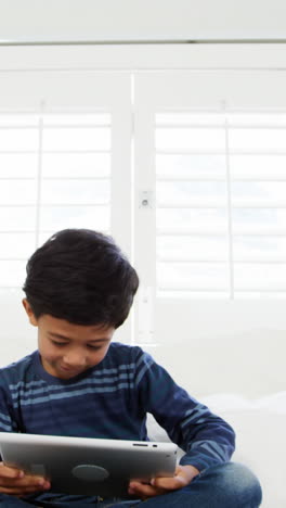 Boy-using-digital-tablet-while-relaxing-on-bed