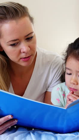 Mother-and-daughter-reading-book-on-bed