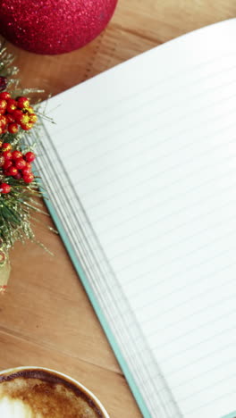 Close-up-of-coffee-cup-with-christmas-decoration-and-notebook