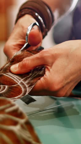 Mid-section-of-craftswoman-cutting-leather-with-scissors