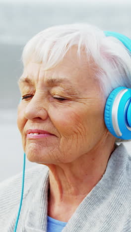 Senior-woman-listening-music-on-headphone-on-beach