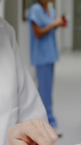 Female-surgeon-checking-medical-reports-while-colleague-discussing-in-background