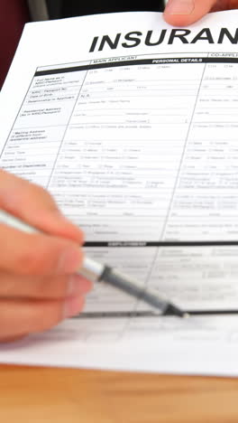 Mid-section-of-businessman-sitting-at-desk-holding-insurance-contract