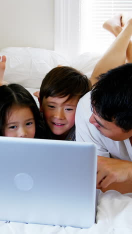 Familia-Feliz-Relajándose-En-La-Cama-Y-Usando-Una-Computadora-Portátil