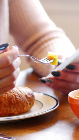 Woman-using-mobile-phone-while-having-breakfast