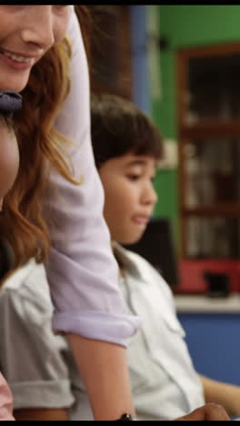 Teacher-assisting-school-kids-on-personal-computer-in-classroom