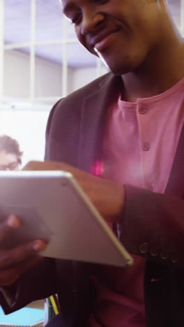 Male-business-executive-using-digital-tablet-while-coworker-interacting-in-background