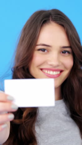 Hermosa-Mujer-Sosteniendo-Una-Tarjeta-De-Visita-En-Blanco-Sobre-Fondo-Azul.