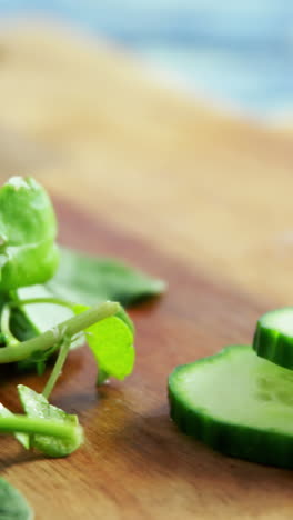 Hierbas-Frescas-Y-Pepino-En-Rodajas-Sobre-Una-Tabla-De-Cortar