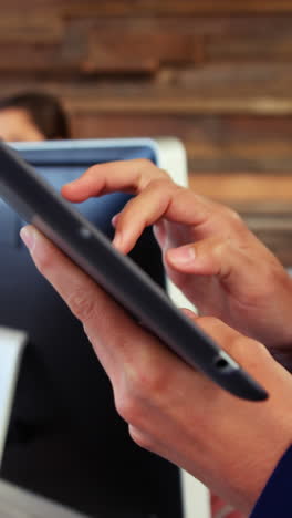 Female-business-executive-using-digital-tablet-while-colleague-working-at-desk