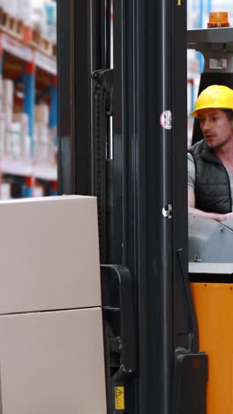 Male-warehouse-worker-using-forklift-truck-for-lifting-stock