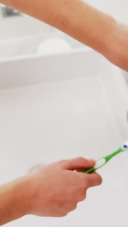 Woman-washing-toothbrush-under-sink-in-bathroom