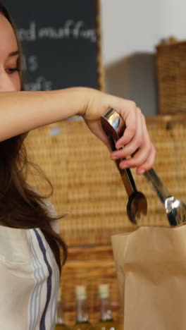 Smiling-female-staff-packing-doughnut-in-paper-bag-at-bakery-section