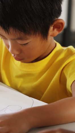 Schoolboy-drawing-in-book-in-classroom