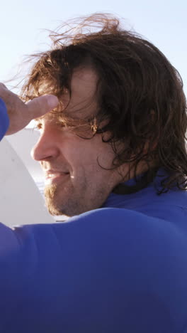 Surfer-with-surfboard-shielding-eyes-at-beach