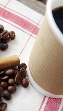 Disposable-cup-with-coffee-beans-and-cinnamon-on-wooden-plank