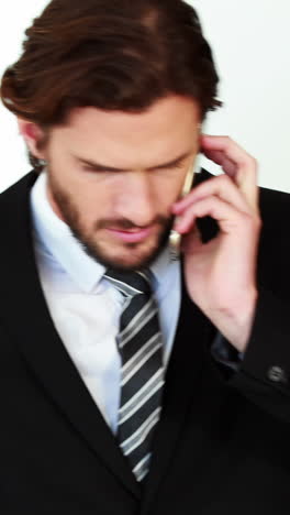 Businessman-talking-on-mobile-phone-while-using-laptop-in-kitchen