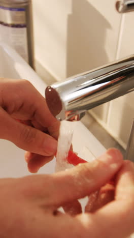 Man-washing-his-toothbrush-under-sink-in-bathroom