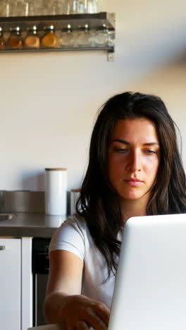 Woman-using-laptop-while-man-drinking-coffee-in-kitchen