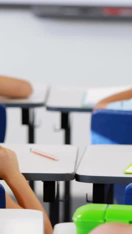 Schoolgirl-whispering-into-her-friend-s-ear-in-classroom