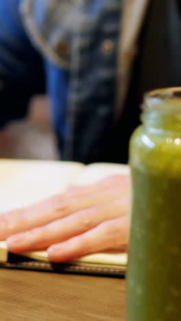 Man-writing-in-his-dairy-with-juice-on-table