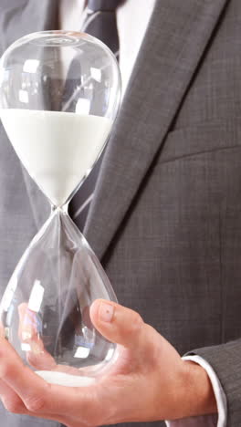 Businessman-holding-sandglass-against-white-background