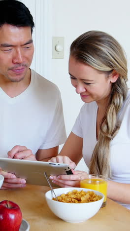 Happy-couple-using-digital-tablet-while-having-breakfast