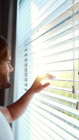 Man-looking-through-window-blinds-after-waking-up