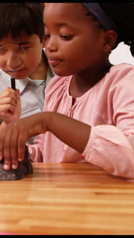 School-kids-looking-at-specimen-stone-through-magnifying-glass-in-laboratory