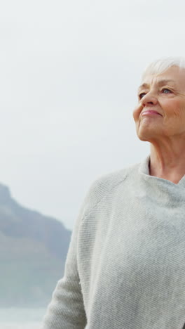 Senior-woman-standing-with-hands-raised-on-beach