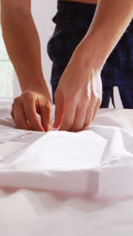 Man-unbuttoning-his-white-shirt-in-bedroom