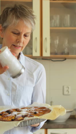 Mujer-Mayor-Rociando-Tarta-Recién-Horneada-Con-Azúcar-En-Polvo