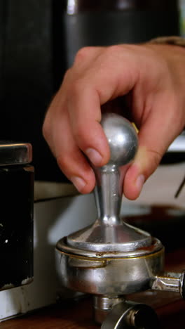 Waiter-pressing-ground-coffee-into-a-portafilter