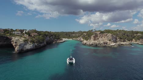 Drone-forward-passing-a-white-docked-sail-boat-in-beautiful-turquoise-lagoon