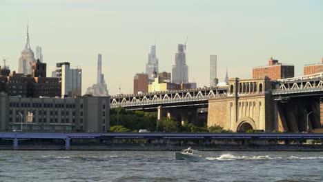 Rascacielos-Del-Centro-De-Manhattan-En-El-Fondo-Vista-Desde-Dumbo-Con-Un-Barco-Abriendo-Camino-En-East-River