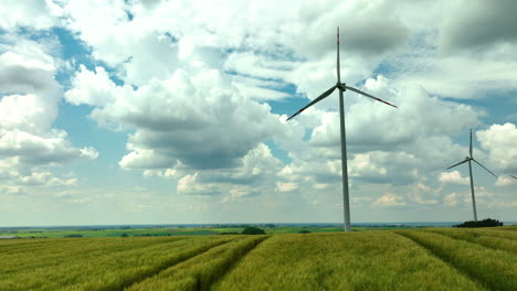 Aerial-footage-capturing-two-wind-turbines-amidst-vast,-golden-fields-under-a-sky-filled-with-dynamic-clouds