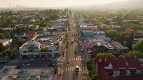 Aerial-Shot-of-Busy-Melrose-Avenue-on-Sunny-Afternoon,-Drone-Footage-Over-Cars-and-Pedestrians-in-Famous-LA-Shopping-District,-Rooftop-Parking-Lots-and-Businesses-Below