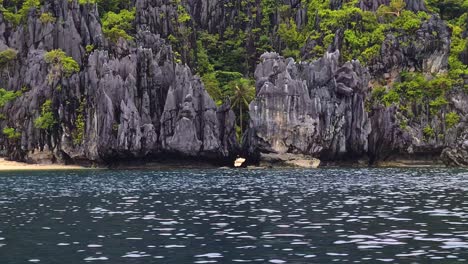 Limestone-Rocks-and-Hidden-Sandy-Beach-Under-Steep-Cliffs-of-Uninhabited-Tropical-Island,-Boat-Passenger-POV