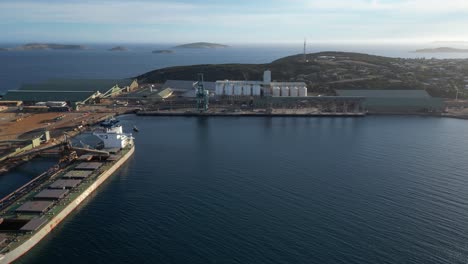 Sea-port-with-oil-tank-and-cargo-ship-docked-near-the-city-with-sky-in-background,-aerial-dynamic