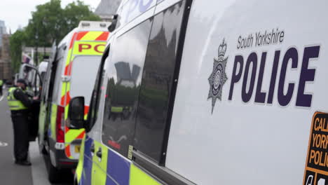 Police-officers-in-riot-uniforms-stand-next-to-a-line-of-police-vans,-one-marked-with-the-words,-“South-Yorkshire-Police”-during-a-major-public-order-event