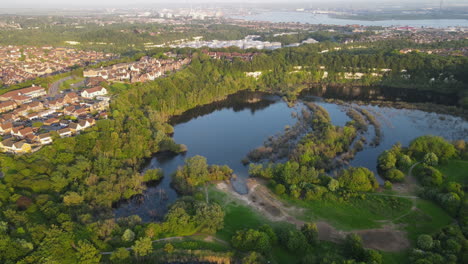 Chafford-gorges-nature-park-with-ponds,-trees,-and-nearby-residential-area,-aerial-view