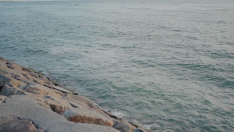 Waves-gently-washing-against-a-rocky-shore-under-a-serene-blue-sky