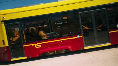 A-vibrant-red-and-yellow-tram-glides-through-Daugavpils-central-square,-revealing-Latgola-Hotel-and-fluttering-Latvian-flags