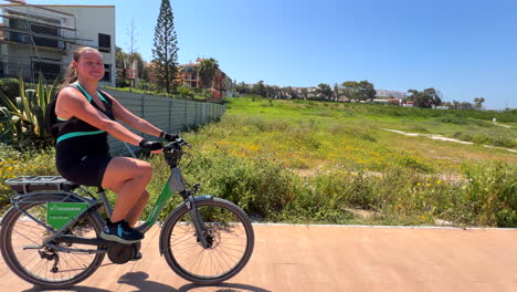 Niña-Feliz-Sonriendo-Y-Montando-Una-Bicicleta-Eléctrica-En-Un-Hermoso-Y-Caluroso-Día-De-Verano-En-Manilva-Marbella-España,-Divertida-Actividad-De-Vacaciones-Soleadas-Cerca-De-La-Playa,-Toma-De-4k