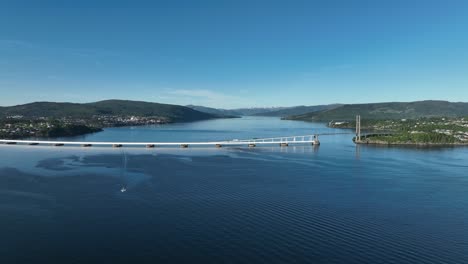 Panoramic-aerial-view-slowly-approaching-Nordhordland-Bridge-from-a-distance,-showing-the-full-bridge-with-Osterfjord-in-the-background